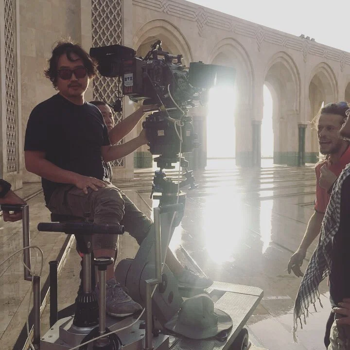 Camera operator on a dolly inside a sunlit arcade during a feature production