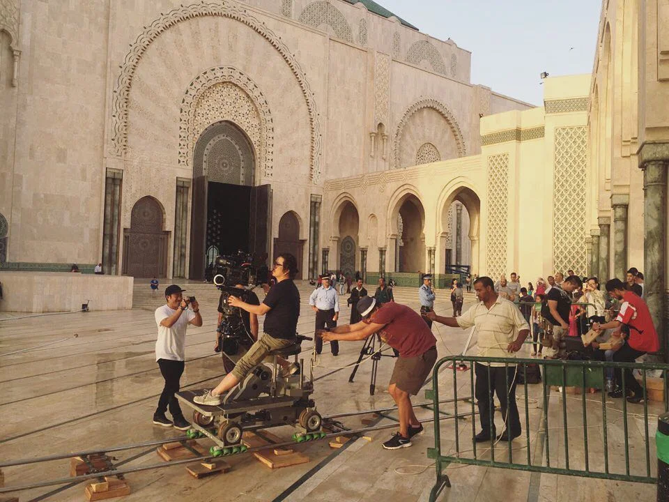 Crew pushing a camera dolly across a plaza in front of a mosque
